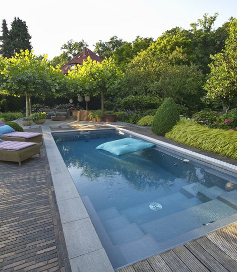 Moderner rechteckiger TeichMeister Swimmingpool in einem gepflegten Garten, umgeben von grünem Pflanzen- und Baumwuchs.